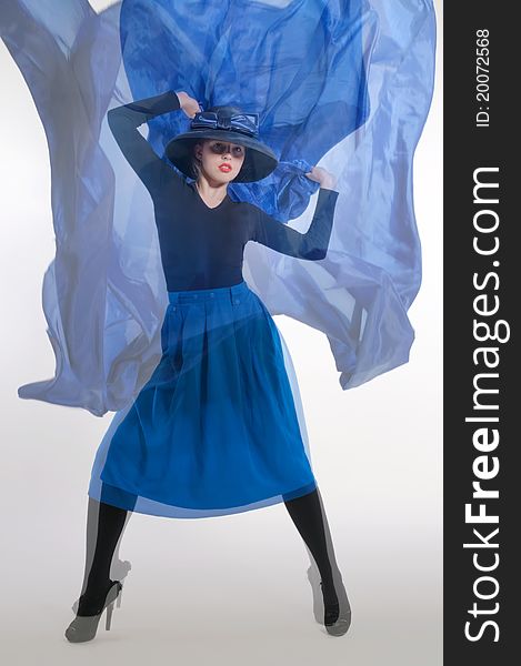 Woman in a dynamic pose, dressed in a blue skirt and a classic hat with a big bow, holding a piece of blue cloth flying. Woman in a dynamic pose, dressed in a blue skirt and a classic hat with a big bow, holding a piece of blue cloth flying.