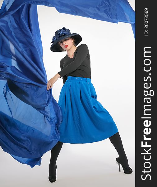 Woman in a dynamic pose, dressed in a blue skirt and a classic hat with a big bow, holding a piece of blue cloth flying. Woman in a dynamic pose, dressed in a blue skirt and a classic hat with a big bow, holding a piece of blue cloth flying.