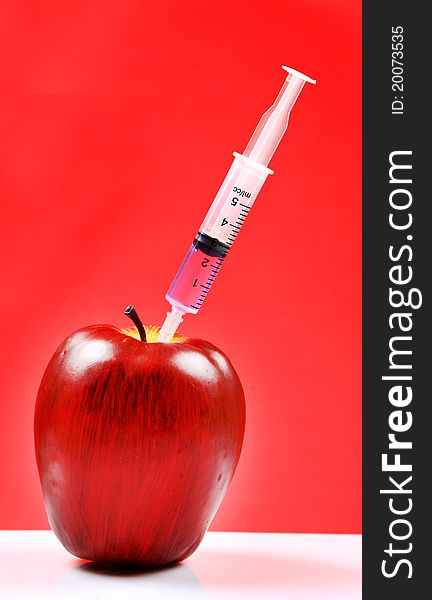 A red apple being injected with syringe containing colour fluid. A red apple being injected with syringe containing colour fluid.