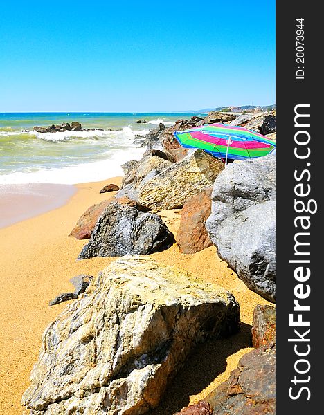 Empty sandy beach with rocks and sun umbrella