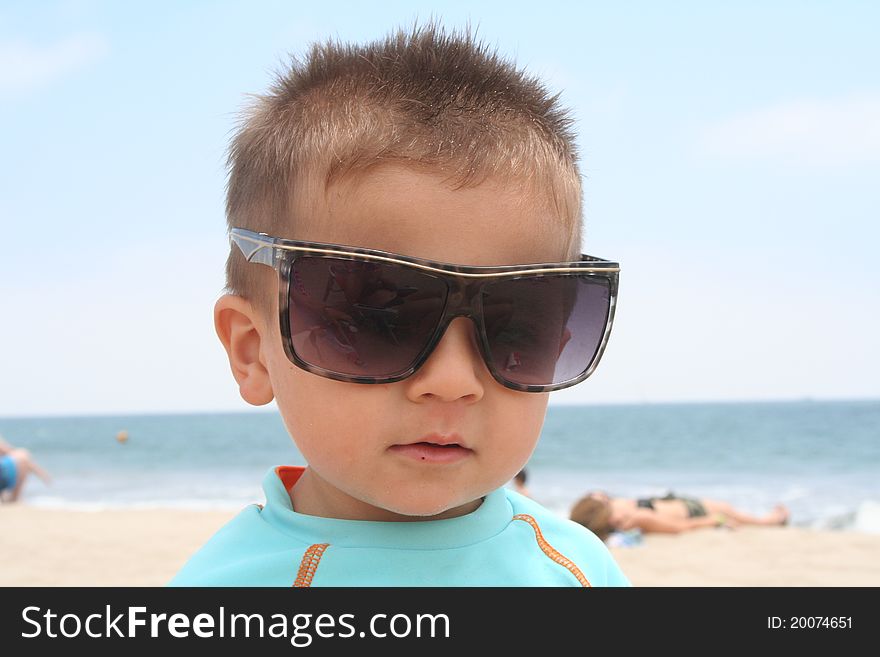 Male todler sitting on the beach wearing sunglasses. Male todler sitting on the beach wearing sunglasses.