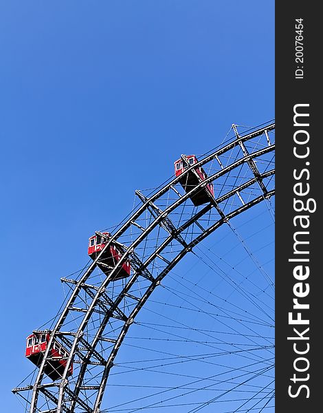 A segment of Vienna's ferris wheel with three cabins against the blue sky