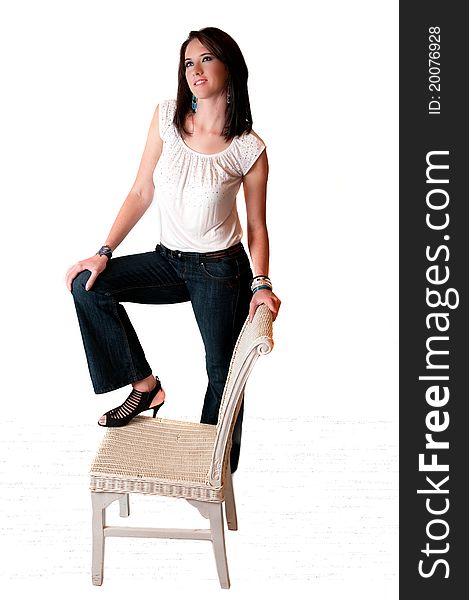 Beautiful brunette model with blue eyes in blue jeans and white blouse standing on a white chair. Beautiful brunette model with blue eyes in blue jeans and white blouse standing on a white chair