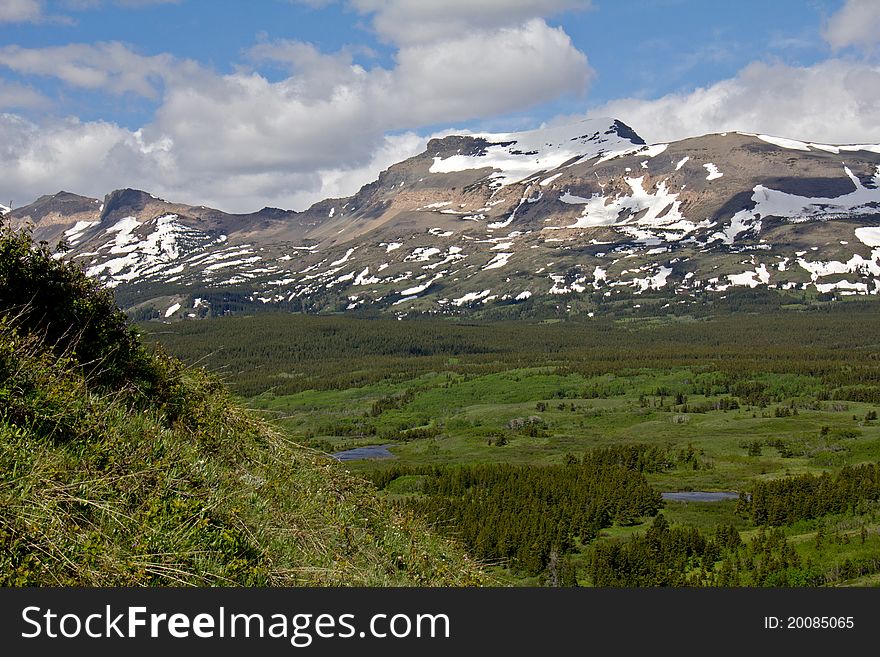 This image shows snowy mountains and a lush valley with several ponds and wetlands in the Glacier National Park area of MT. This image shows snowy mountains and a lush valley with several ponds and wetlands in the Glacier National Park area of MT.