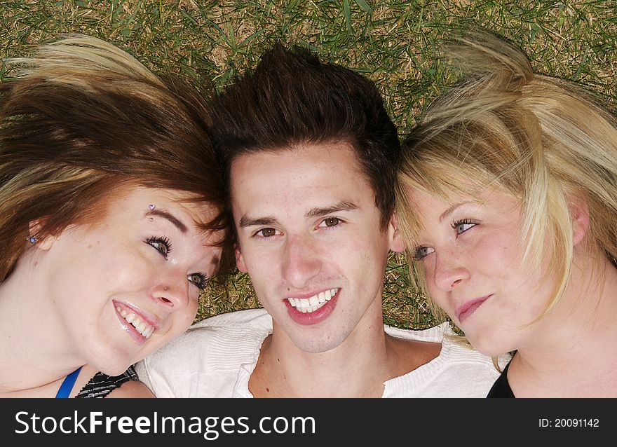 Lucky guy with two adoring girlfriends, close up, head shots. Guy smiling at camera, girls smiling at him. Happy teens laying on grass. Lucky guy with two adoring girlfriends, close up, head shots. Guy smiling at camera, girls smiling at him. Happy teens laying on grass