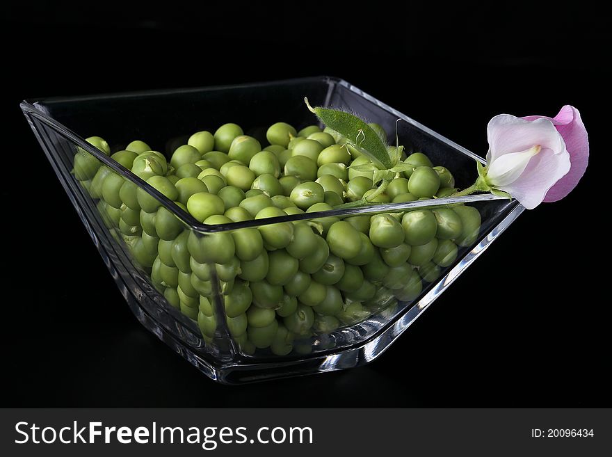 Fresh peas in a glass vase on a black background