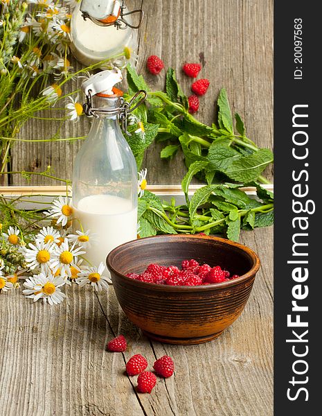 Composition with bowl of fresh ripe raspberries,bottle of milk and bunch of camomile on old wooden table, near mirror with reflex