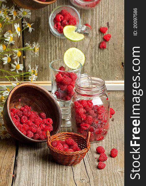 Composition with fresh ripe raspberries in glass, pot, bowl and basket on old wooden table, near mirror with reflex