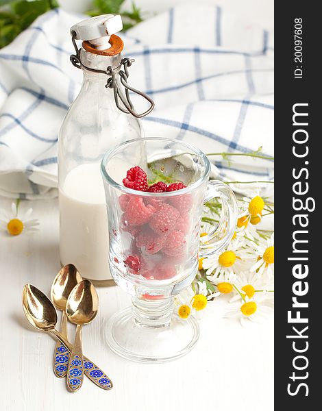 Still-life with fresh ripe raspberries in glass, bottle of milk and bunch of camomile flowers. Still-life with fresh ripe raspberries in glass, bottle of milk and bunch of camomile flowers