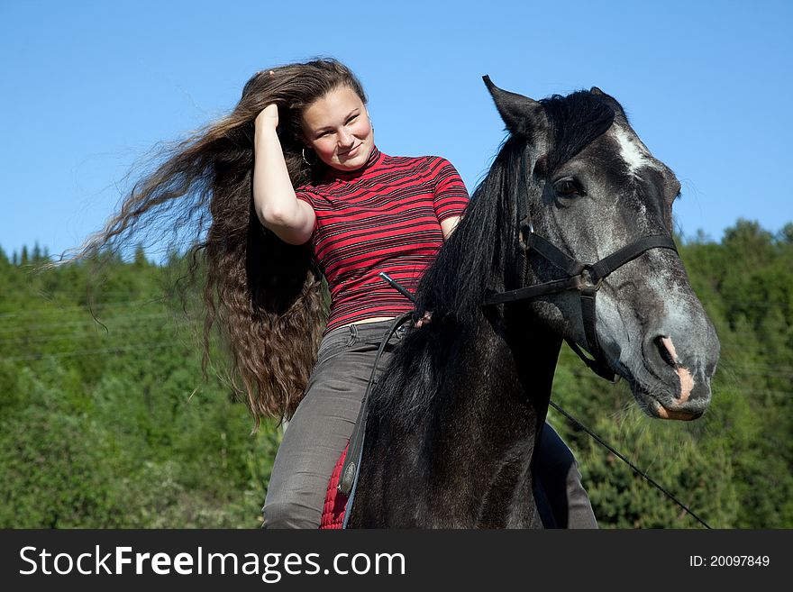 A girl with flowing hair on a black horse in a forest