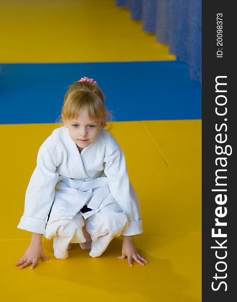 The little girl in a white kimono sits on the mat. The little girl in a white kimono sits on the mat