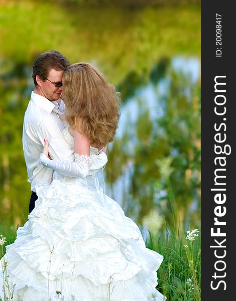 Bride and groom hugging each other in the tall grass by the lake. Bride and groom hugging each other in the tall grass by the lake