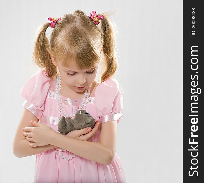 The little girl in a pink dress on a light gray background lulls toy. The little girl in a pink dress on a light gray background lulls toy