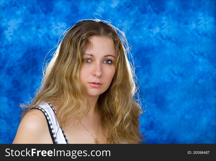 Young pretty girl with long blond hair on a blue background quietly watching us. Young pretty girl with long blond hair on a blue background quietly watching us