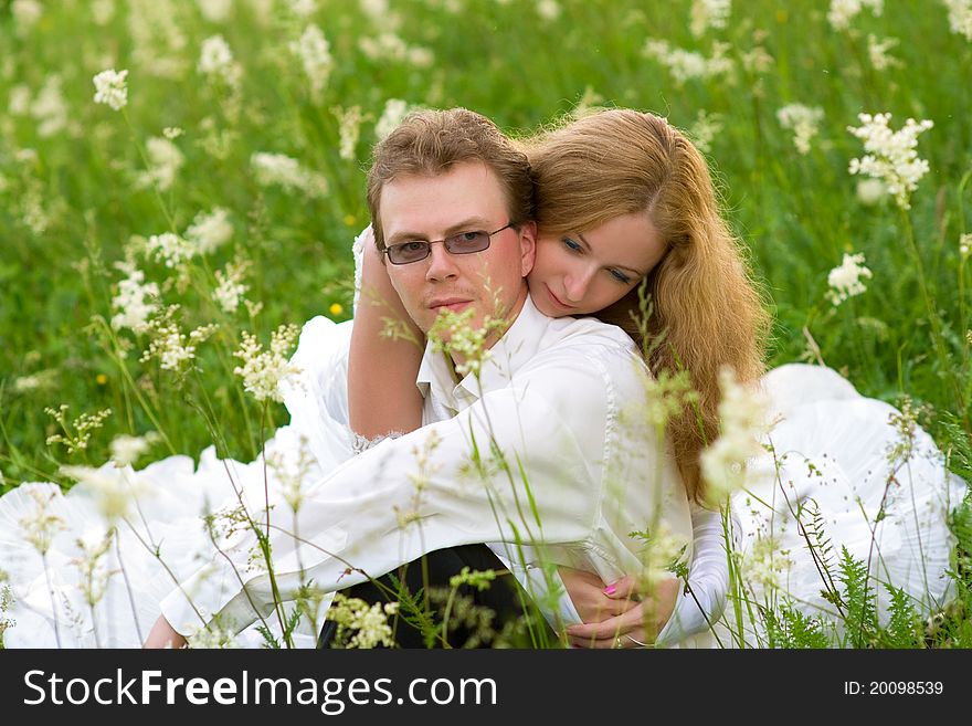 In the high green grass among the white flowers sitting in love newlyweds. In the high green grass among the white flowers sitting in love newlyweds