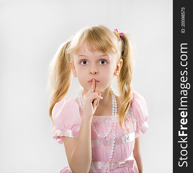 A little girl with long blond hair in a smart pink dress put her finger to her lips. A little girl with long blond hair in a smart pink dress put her finger to her lips