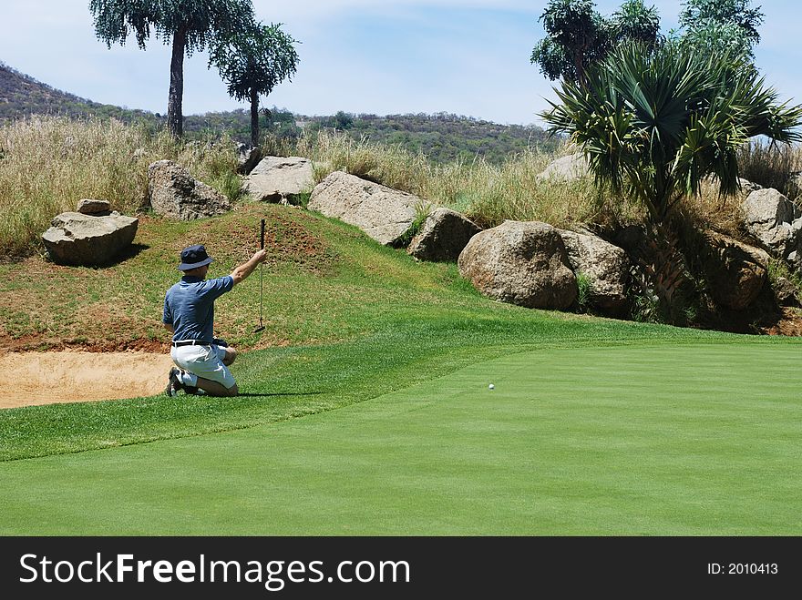 Middle age golfer sitting down next to the green, estimating the line for the putt. Middle age golfer sitting down next to the green, estimating the line for the putt.