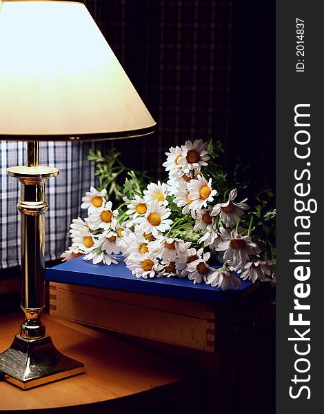Lamp and daisies on a wooden desk in the evening
