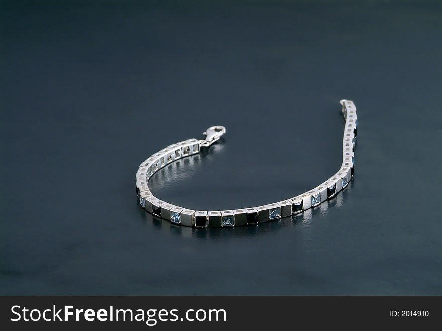 Silver bracelet with precious stones on a dark gray/green background.