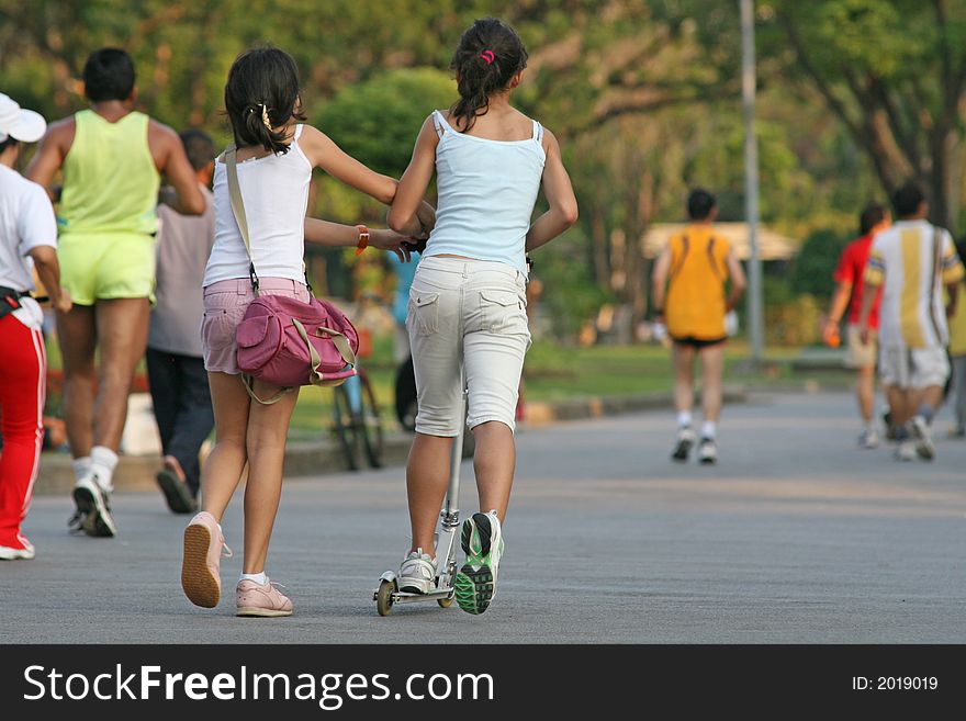 Two young girls playing on a scooter in the park