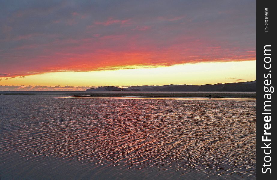 Sunset on seal. Dark clouds. The red and yellow highlights on water are on foreground. Islands and capes are on background. Russian Far East, Primorye, Japanese sea, Sokolovskaya bay, Petrova and Belcova islands.