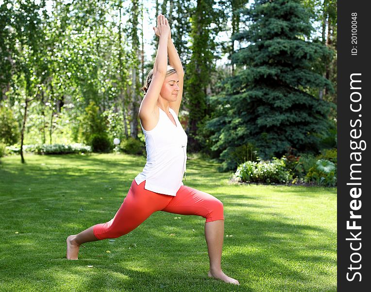 Young girl in a white shirt and red pants doing yoga outdoors