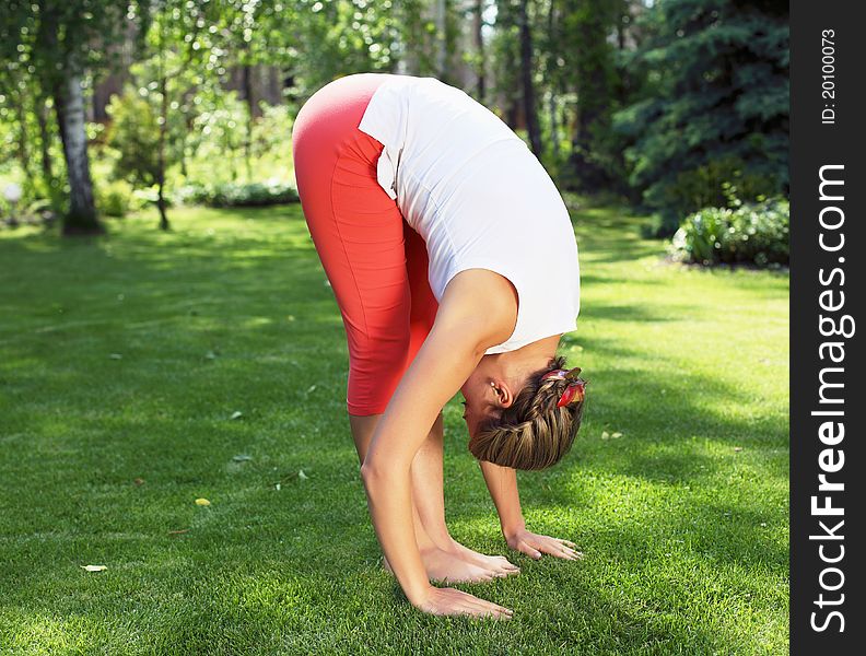 Young girl in a white shirt and red pants doing yoga outdoors