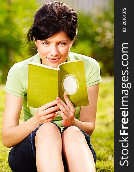 Caucasian woman is reading the green book sitting on the grass in the park. Caucasian woman is reading the green book sitting on the grass in the park