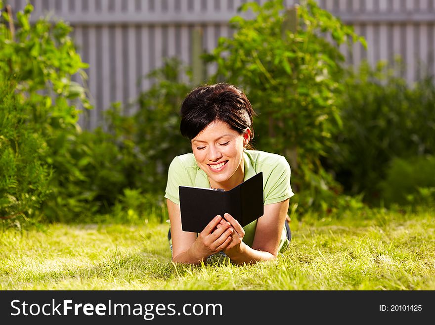 Caucasian woman is reading the green book sitting on the grass in the park. Caucasian woman is reading the green book sitting on the grass in the park