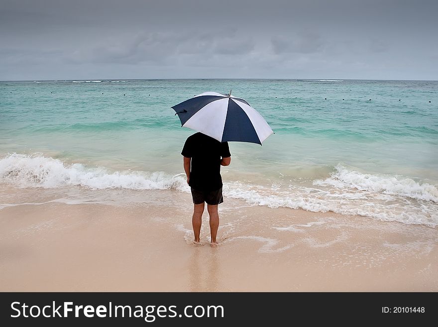 Tanned man stand with umbrella in blue sea under grey cloud sky