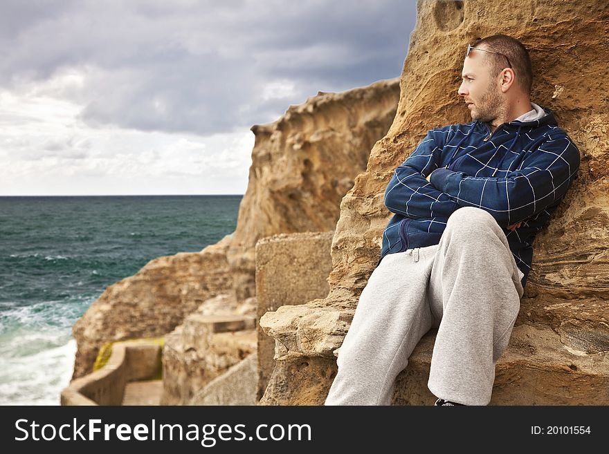 Man laying on the rocks on the beach looking toward the sunlit water pensively. Man laying on the rocks on the beach looking toward the sunlit water pensively