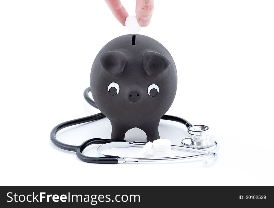 Putting pills on a piggy bank with stethoscope isolated on white