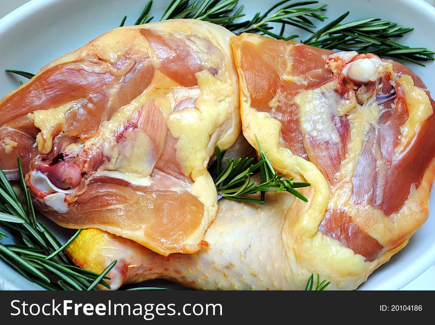 Raw chicken legs with rosemary on white dish