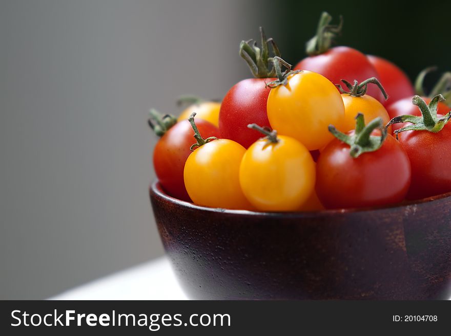 Cherry tomatoes in a dark colored bowl on a white surface with copy spaces and limited focus. Cherry tomatoes in a dark colored bowl on a white surface with copy spaces and limited focus.