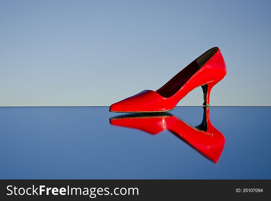One red stiletto on mirror and sky background