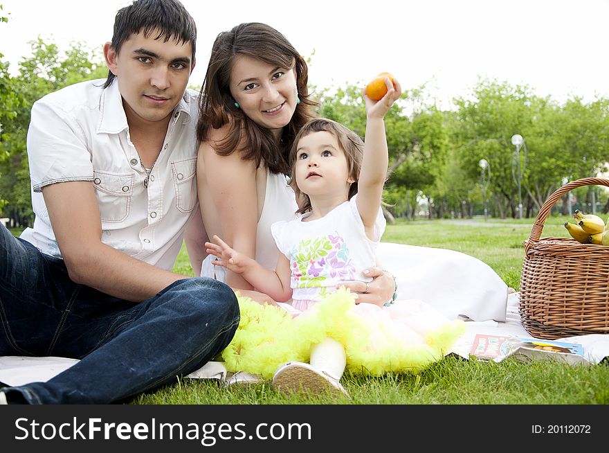 The husband, the wife and the child sit on a coverlet in park. The husband, the wife and the child sit on a coverlet in park