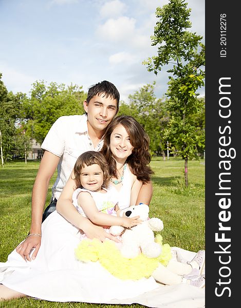 The husband, the wife and the child sit on a coverlet in park