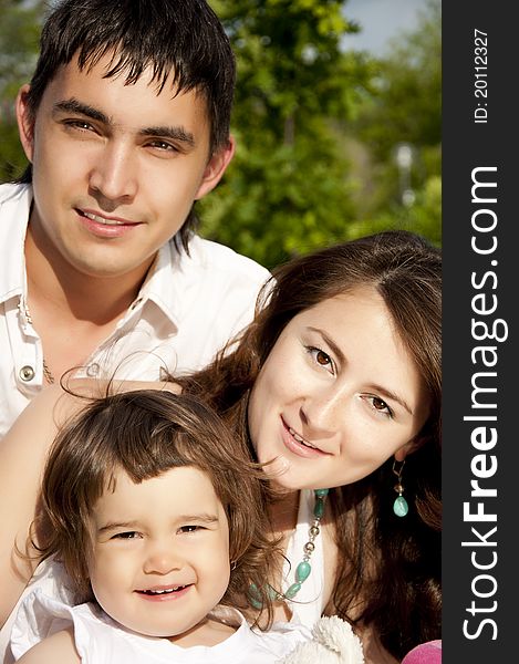 The husband, the wife and the child sit on a coverlet in park