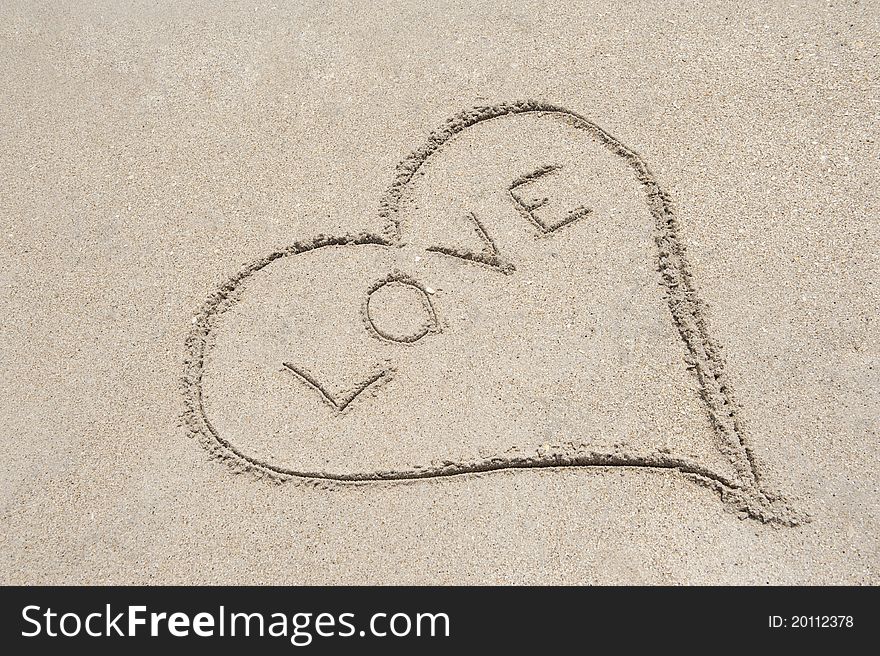 A heart shape drawn in the sand with the word LOVE written in the middle. A heart shape drawn in the sand with the word LOVE written in the middle