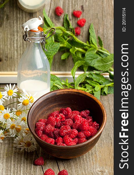 Bowl of fresh ripe raspberries, bottle of milk and mint's leafes near mirror with reflection on old wooden table. Bowl of fresh ripe raspberries, bottle of milk and mint's leafes near mirror with reflection on old wooden table