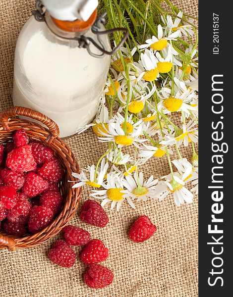 Top view on basket of fresh ripe raspberries, bottle of milk and camomile flowers on sacking. Top view on basket of fresh ripe raspberries, bottle of milk and camomile flowers on sacking