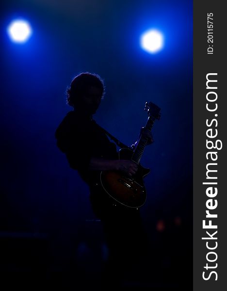 A silhouette of a musician with a guitar in bright concert light. A silhouette of a musician with a guitar in bright concert light