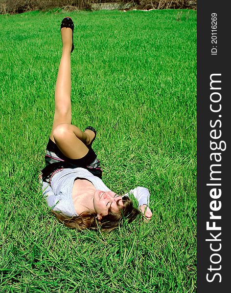 Smiling lady laying on a green grass holding and stretching her leg up. Smiling lady laying on a green grass holding and stretching her leg up