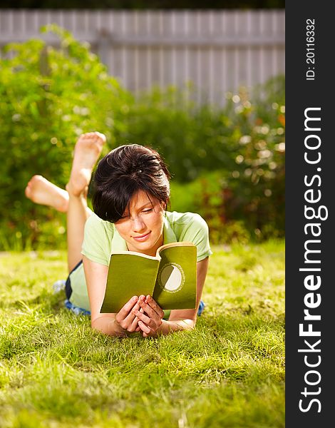 Caucasian woman is reading the green book lying on the grass in the park. Caucasian woman is reading the green book lying on the grass in the park