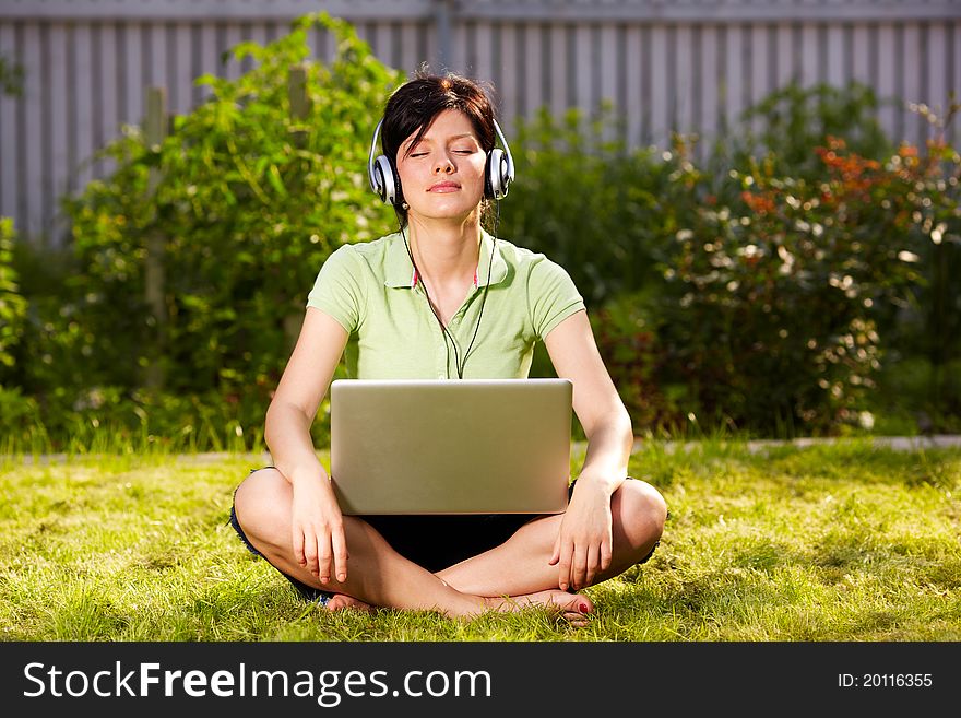 Caucasian woman is sitting on the grass wearing headphones. Caucasian woman is sitting on the grass wearing headphones