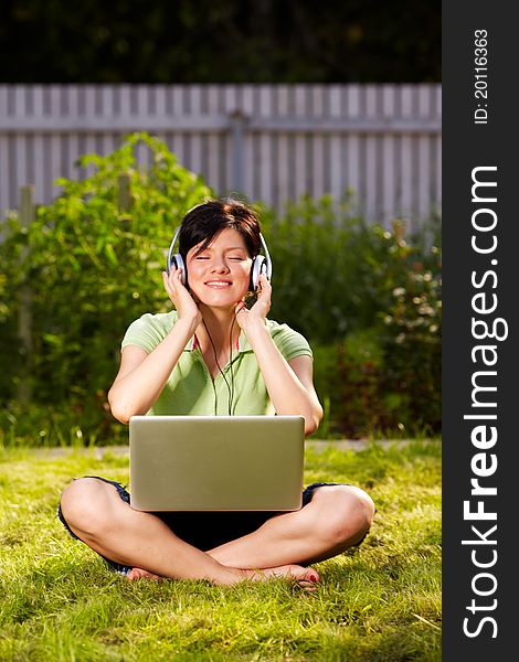 Caucasian woman is sitting on the grass wearing headphones. Caucasian woman is sitting on the grass wearing headphones
