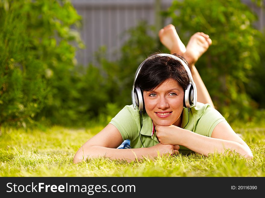 Caucasian woman is lying on the grass wearing headphones. Caucasian woman is lying on the grass wearing headphones