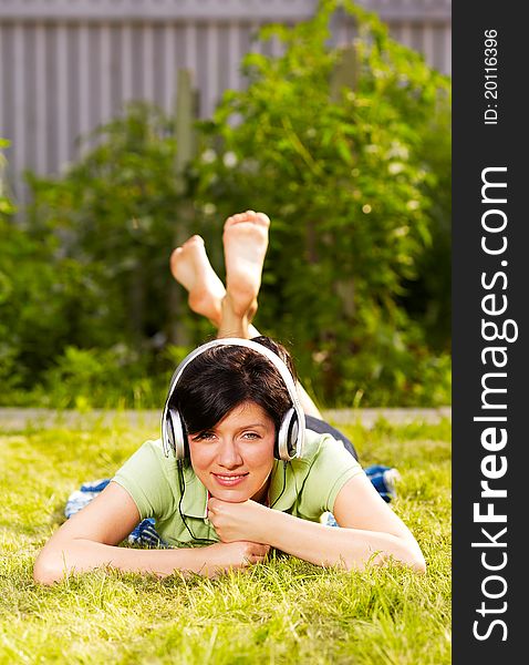 Caucasian woman is lying on the grass wearing headphones. Caucasian woman is lying on the grass wearing headphones