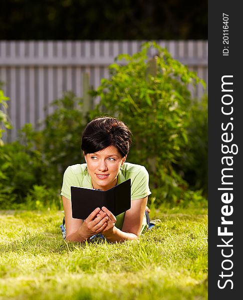 Caucasian woman is reading the e-book lying on the grass in the park. Caucasian woman is reading the e-book lying on the grass in the park