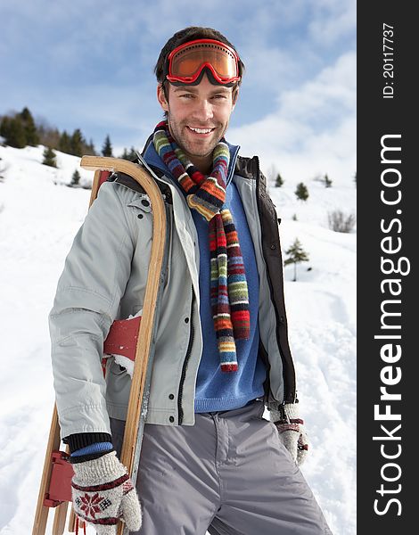 Young Man Carrying Sled In Alpine Landscape smiling at camera